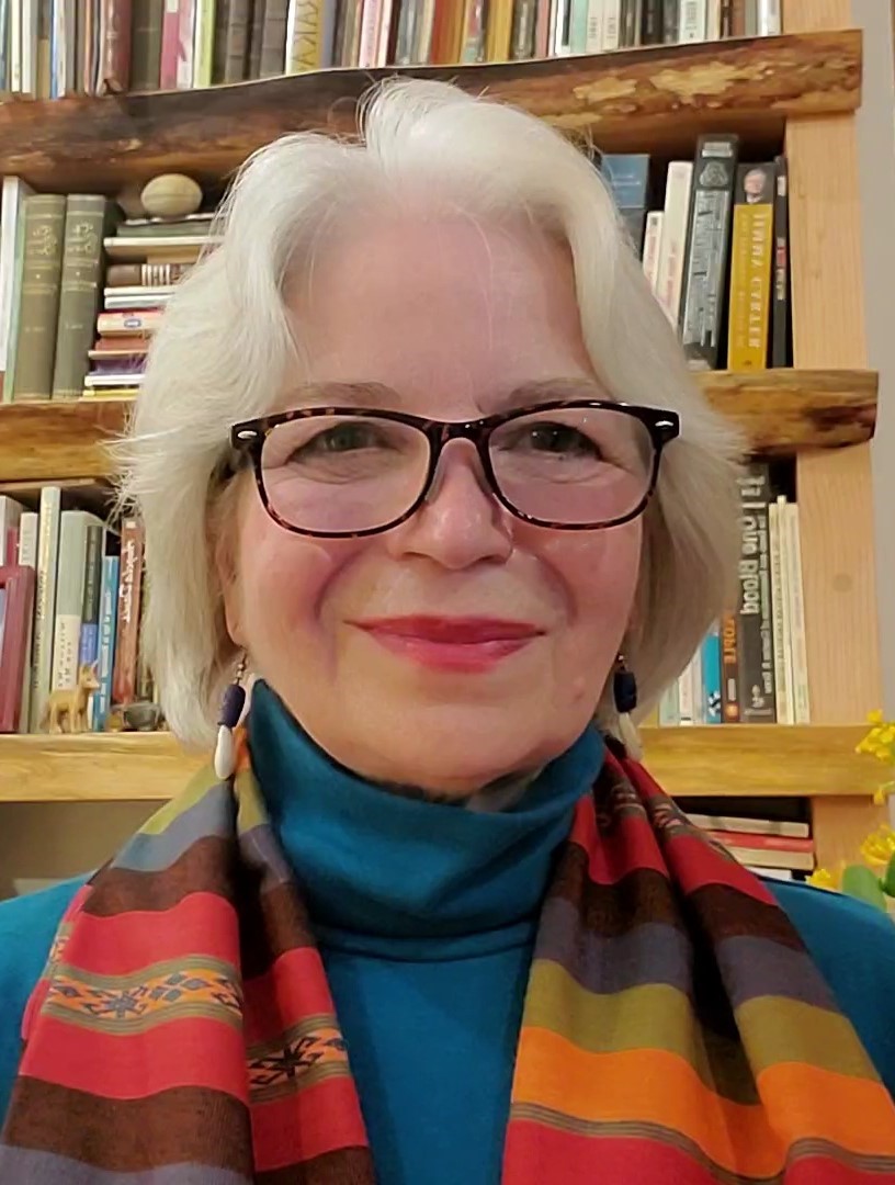 Image of a white woman with white hair wearing a colorful scarf, blue shirt, and tortoise shell spectacles