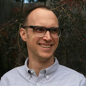 White man with ombre colored spectacles and a blue button-down shirt