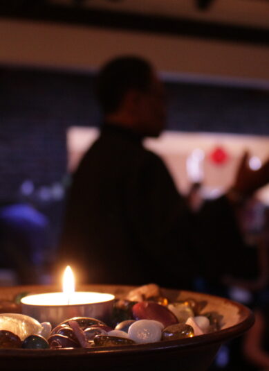 Image of a lit chalice in the foreground with a black minister preaching in the background