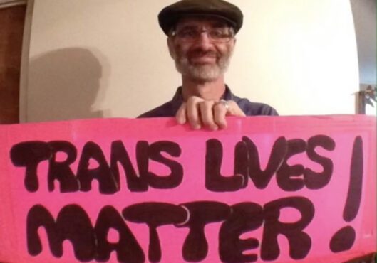 White man holding sign that reads "Trans Lives Matter!"