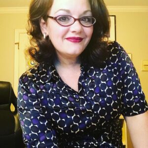 White woman woman spectacles, red lipstick, and blue and purple blouse