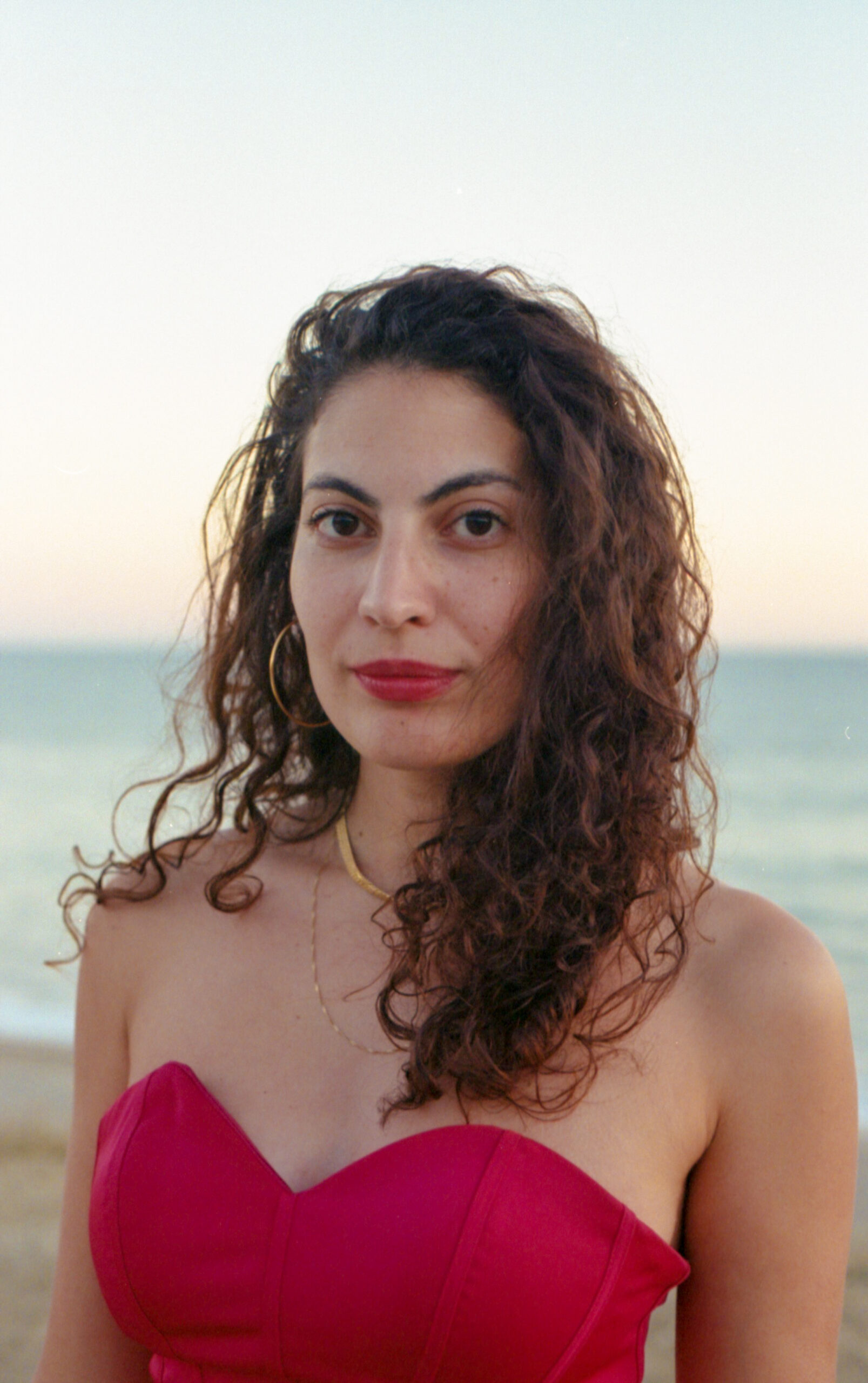Image of a Arab Jewish woman with cold jewelry and red outfit set in front of ocean view