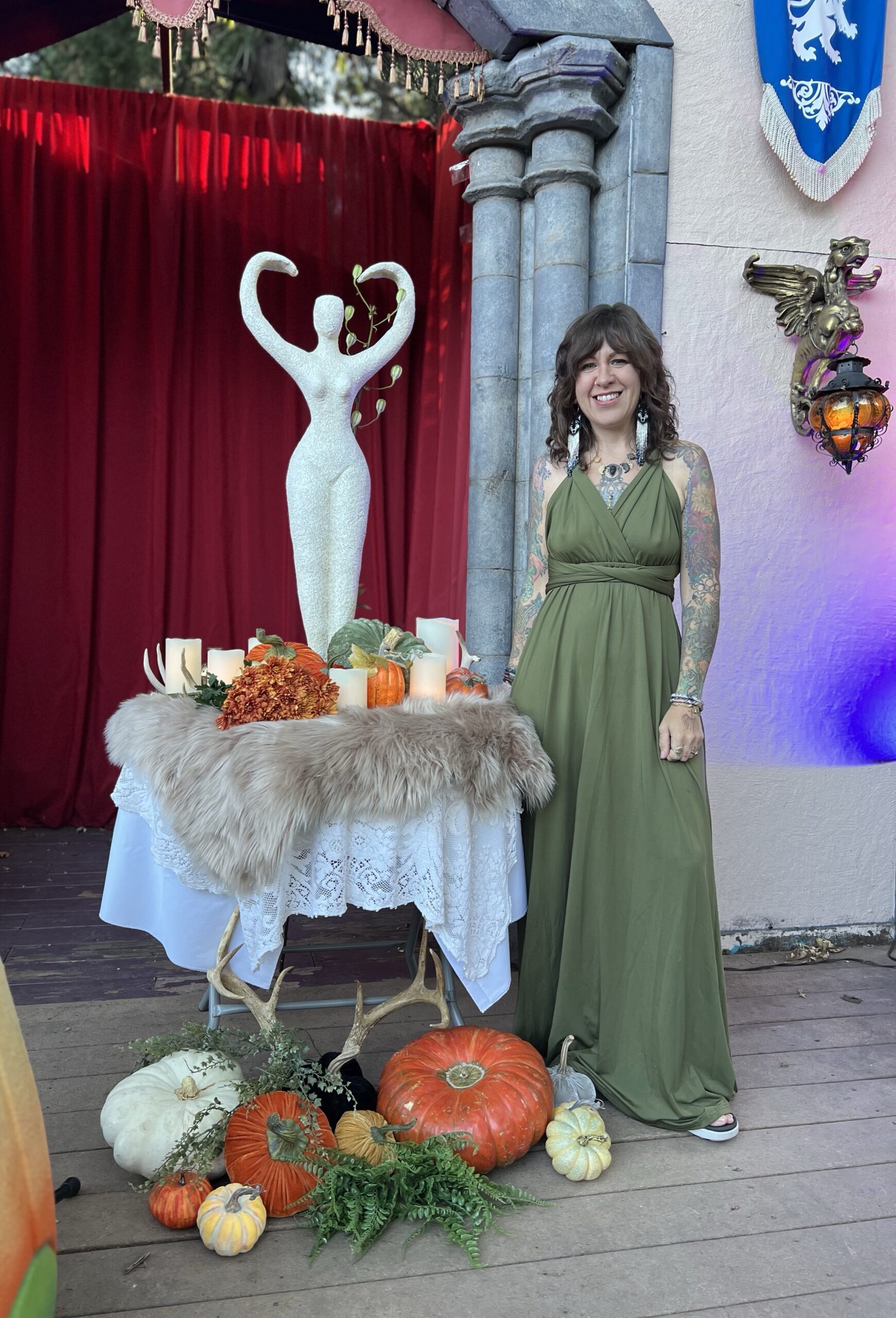 Beautiful white woman in a green dress standing next to woman-centric autumnal altar